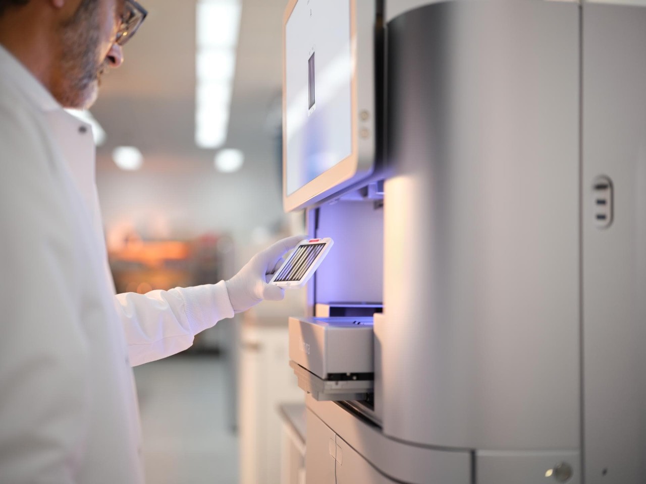 Profile image of a male scientist examining a 25B flow cell cartridge before inserting into a NovaSeq X drawer.